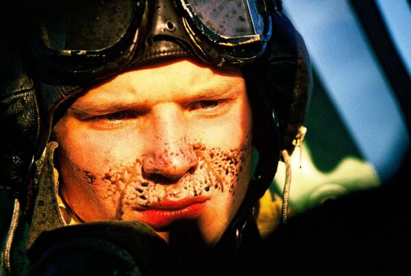 Close-up of a Czechoslovak RAF pilot's face, oil-spattered, goggles pushed up on his flying helmet.