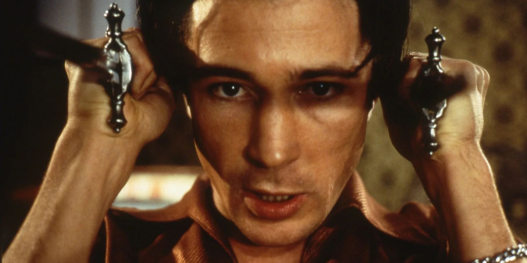 Mojo — a man holding two candlesticks to his head, in close-up